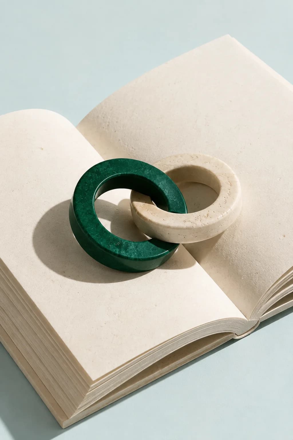 Livro aberto com dois anéis de precisão interligados, em verde e marfim.